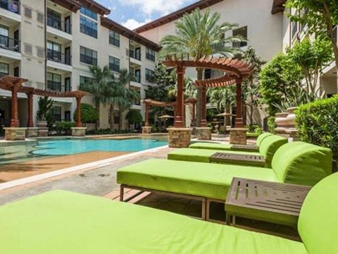 a large swimming pool with green lounge chairs in front of a building