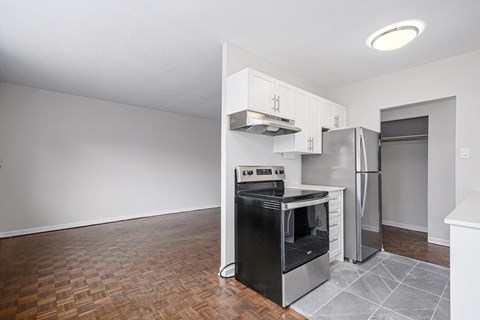 an empty living room with a kitchen with a stove and refrigerator