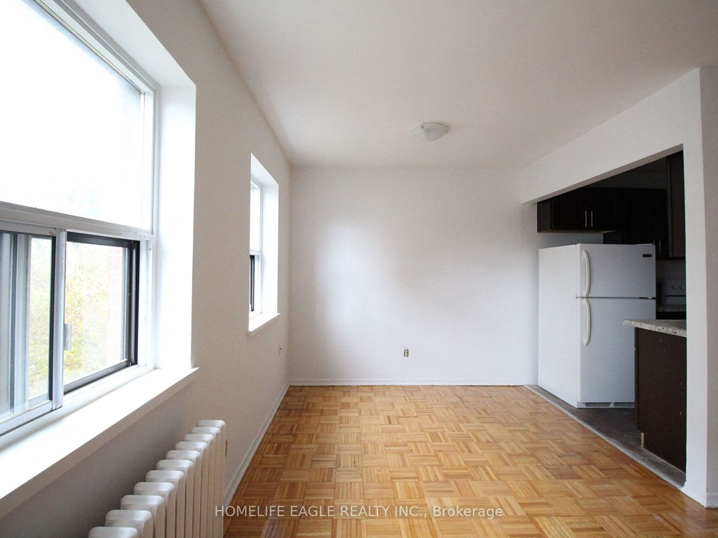 an empty living room with a large window and a white refrigerator