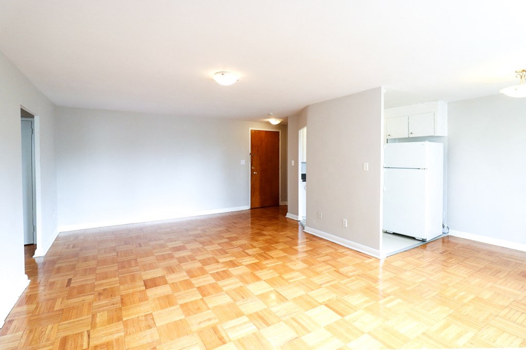 an empty living room with a wood floor and a refrigerator