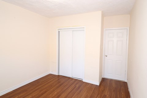 a bedroom with white walls and a wooden floor and a closet