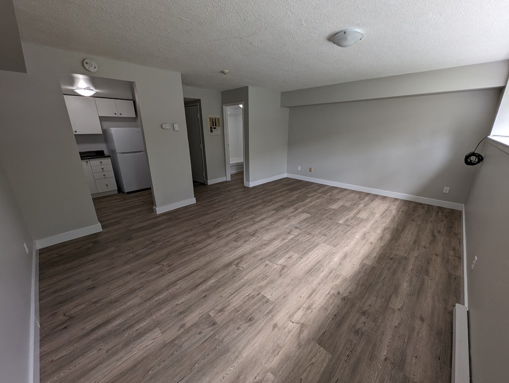 an empty living room with wood floors and a kitchen