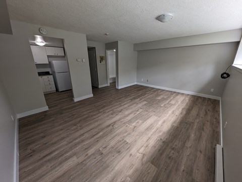 an empty living room with wood floors and a kitchen