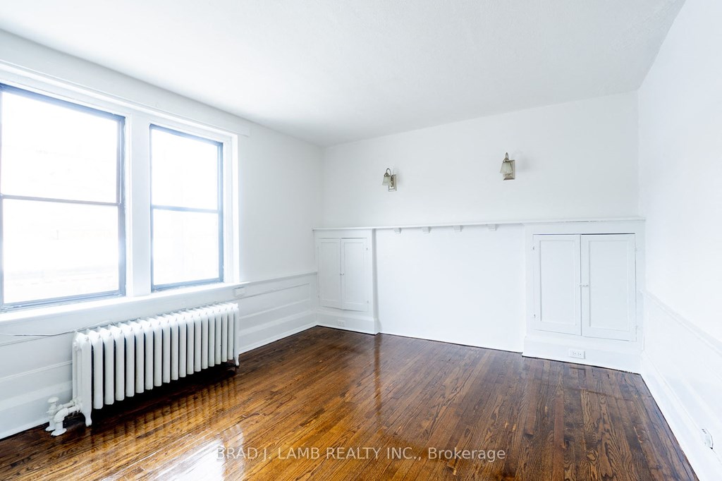 bedroom with wood floors and white walls and a radiator and two windows