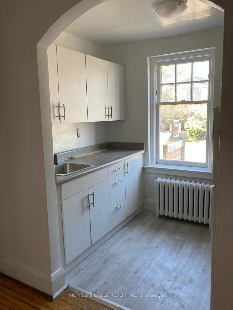an empty kitchen with white cabinets and a window
