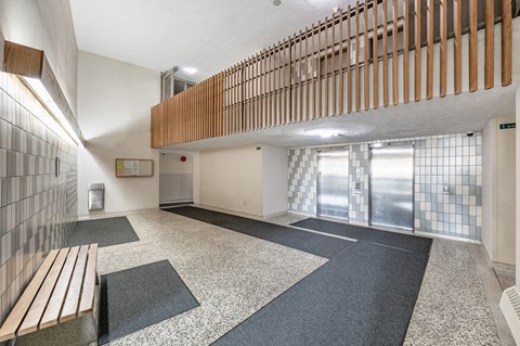 A hallway with a bench, tile floors, and a wooden railing.