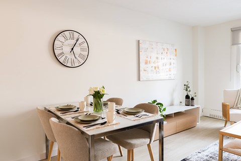 A dining room with a table set for two and a clock on the wall.