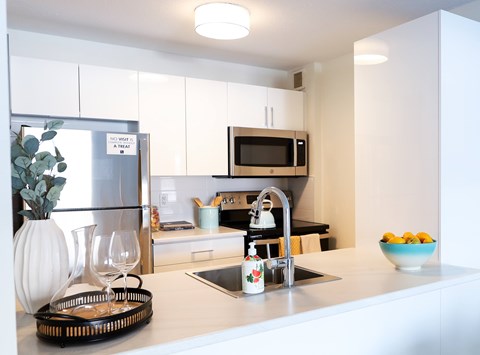 A modern kitchen with a white fridge, microwave, and a bowl of fruit on the counter.