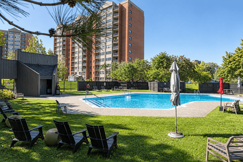 A pool surrounded by lawn chairs and umbrellas with a tall building in the background.