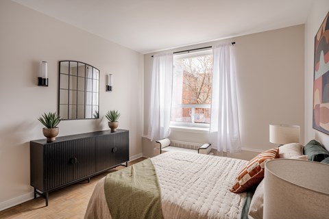 A bedroom with a bed, nightstand, and a window with curtains.
