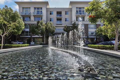 A fountain in the middle of a paved area in front of a building.