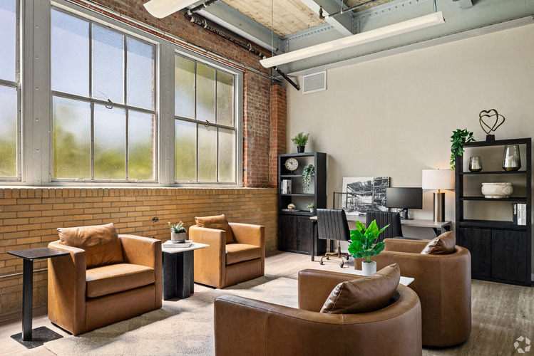 A living room with brown leather furniture and a brick wall.