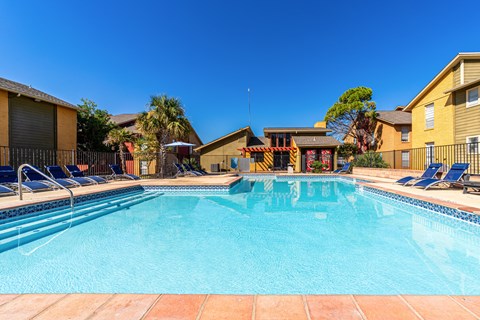 A swimming pool surrounded by lounge chairs and apartment buildings.