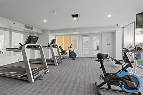 A gym with treadmills, exercise bikes, and a television.