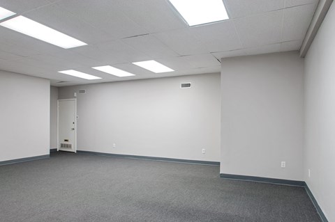 A white room with a carpeted floor and a door on the left side.