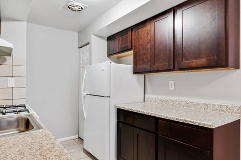 A kitchen with a white refrigerator and brown cabinets.