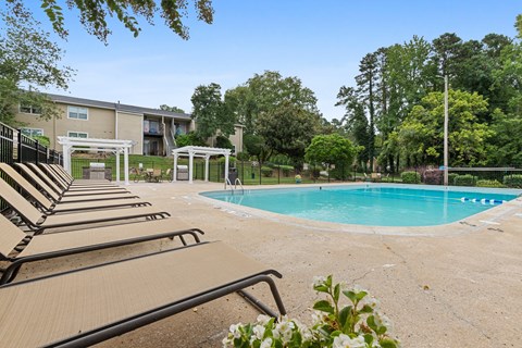A pool area with sun loungers and a building in the background.