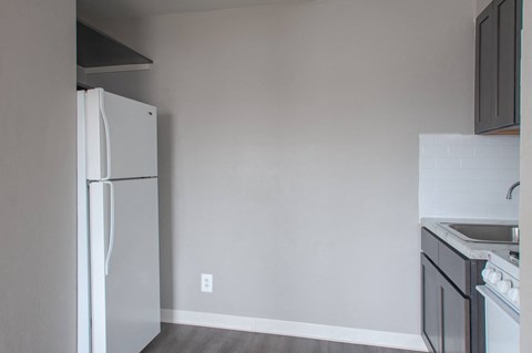 A white refrigerator stands in a kitchen with a white stove and sink.