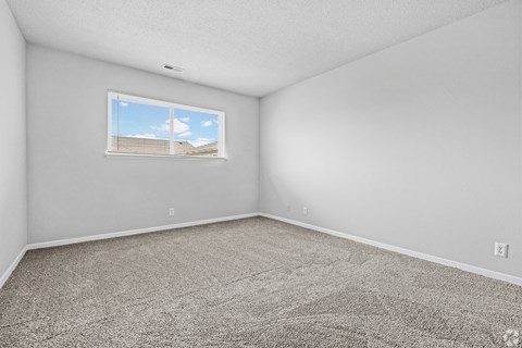 A room with a carpeted floor and a window showing a building outside.