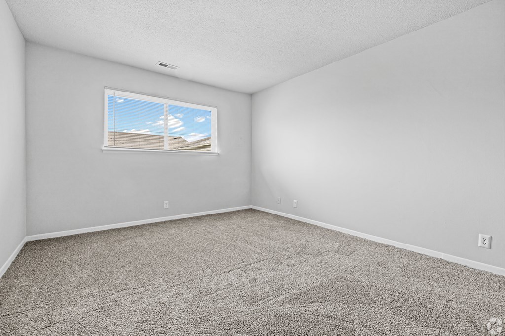 A room with a carpeted floor and a window showing a building outside.