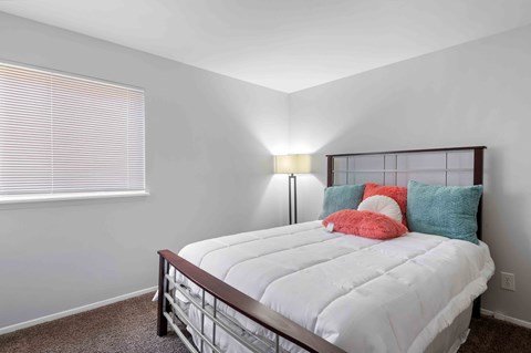 A bedroom with a white bed and a window with blinds.