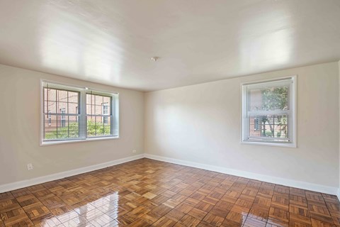 A room with wooden flooring and two windows.