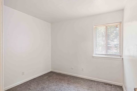 A room with a carpeted floor and a window with blinds.