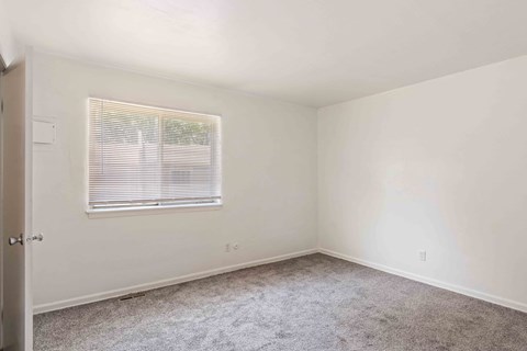 A room with a carpeted floor and a window with blinds.