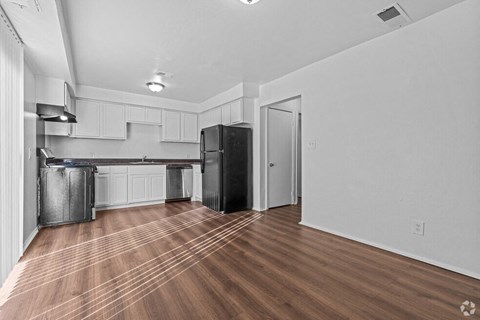 A kitchen with a black refrigerator and wooden floors.