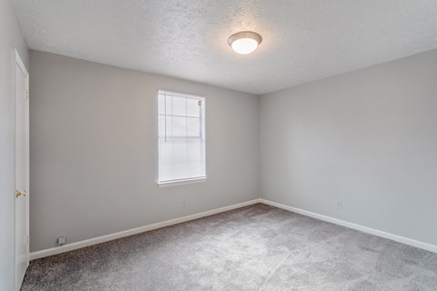 A room with a window and a carpeted floor.