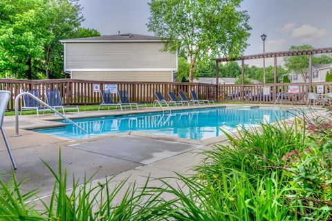 A pool surrounded by chairs and greenery.