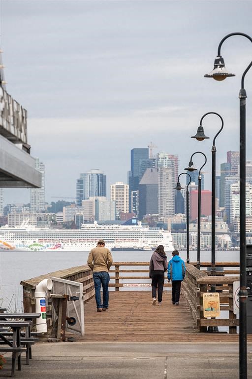three people walking down a pier with a city in the background