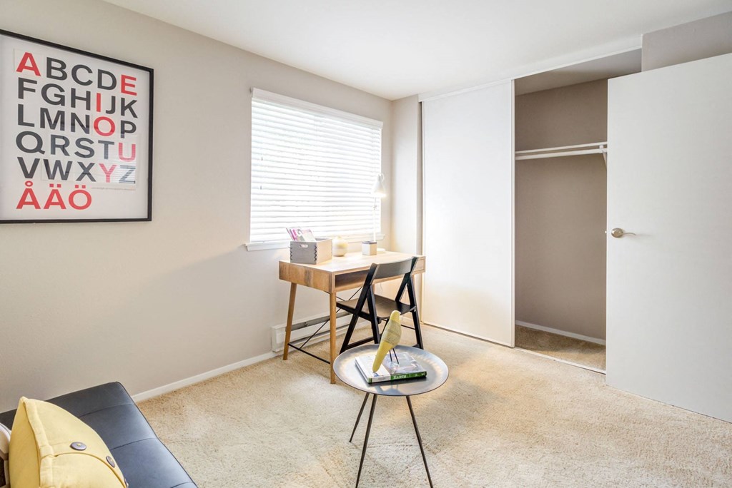 a living room with a desk and chair and a door to a closet