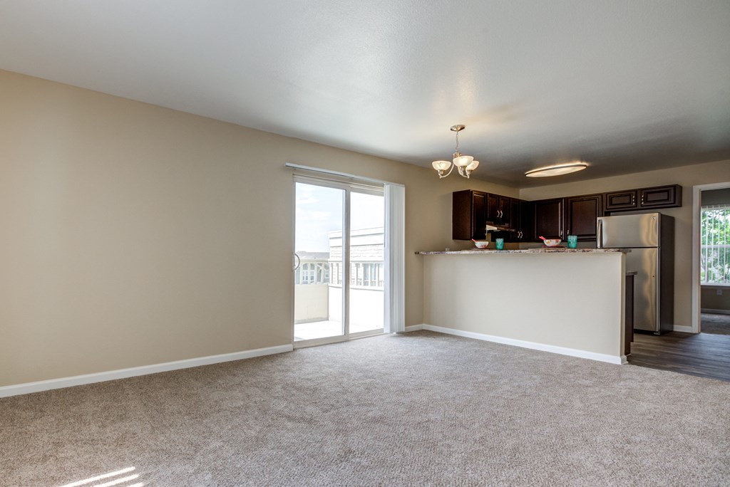 an empty living room with a kitchen and a door to a balcony