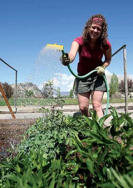 a woman is watering a garden with a green hose