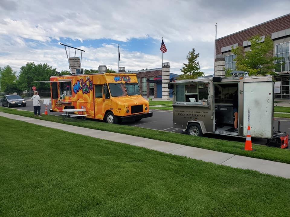 a yellow food truck parked next to a silver food truck