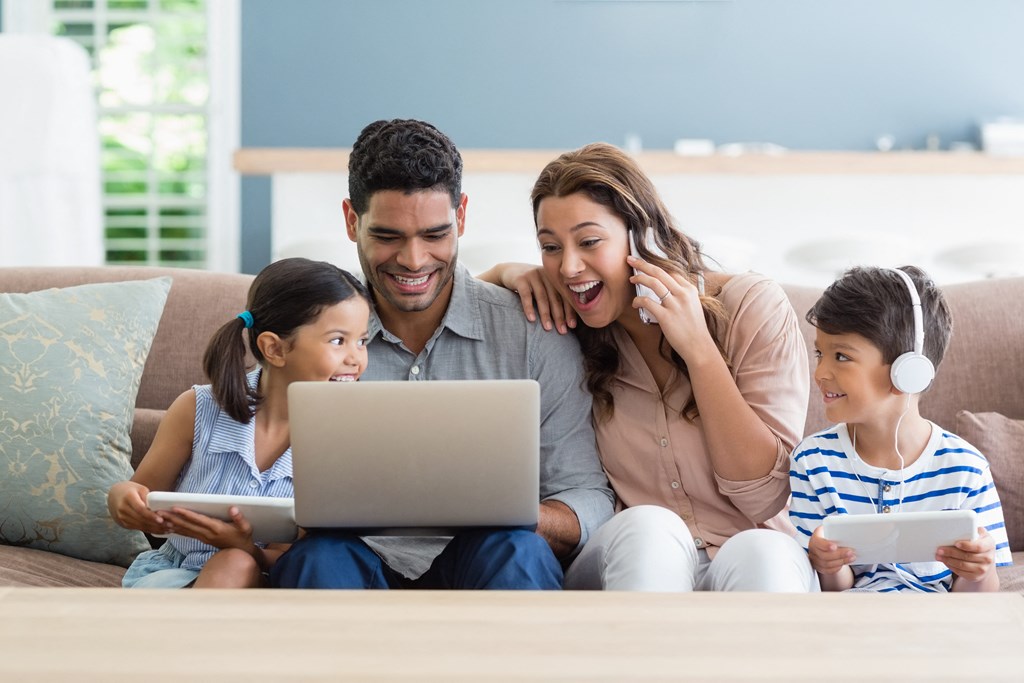 a family sitting on a couch using a laptop computer and listening to headphones