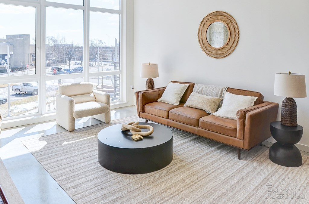 A living room with a brown couch, a white chair, and a round table with a yellow object on it at The Anthem at Square 10 Apartments, New Haven, CT