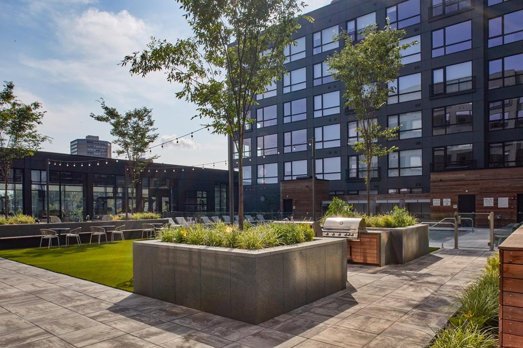 A modern building with a large glass facade and a courtyard with concrete planters and greenery at The Anthem at Square 10 Apartments, New Haven, Connecticut