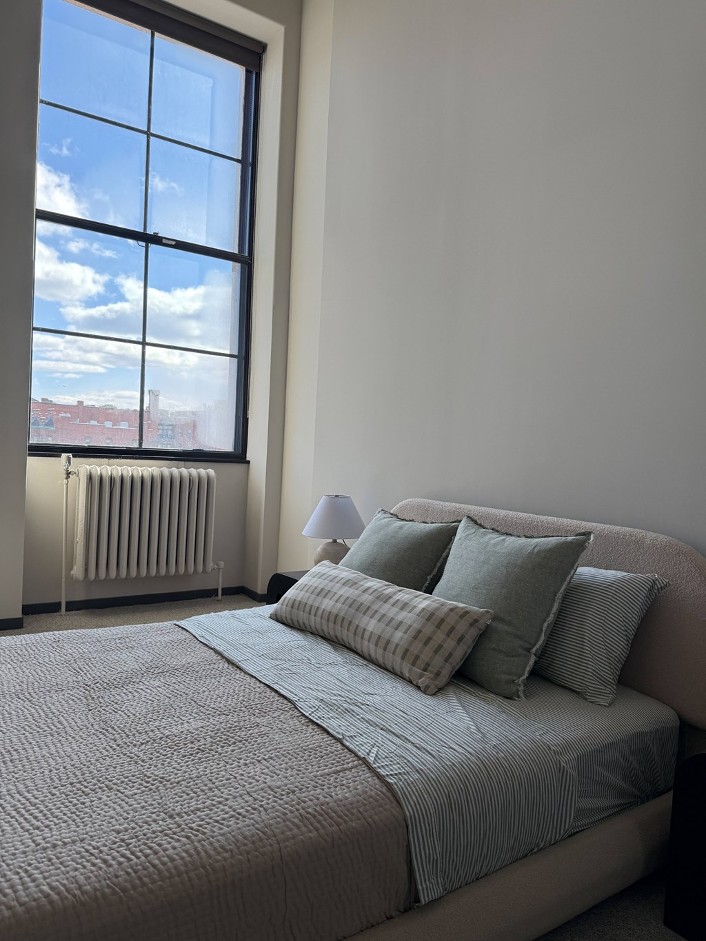 A bed with a grey comforter and pillows is in front of a window. at The 55 Elm Club Apartments, Hartford, CT, 06106