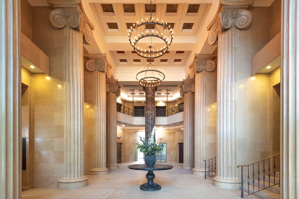 A large, ornate chandelier hangs from the ceiling in a grand hallway with columns on either side.
