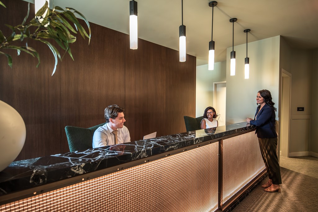 A reception area with a man and woman sitting behind the desk and a woman standing at the front.