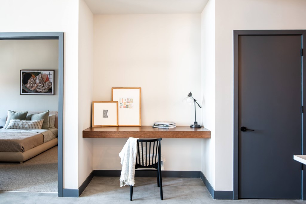 A room with a bed, a desk with a chair and a shelf with picture frames.