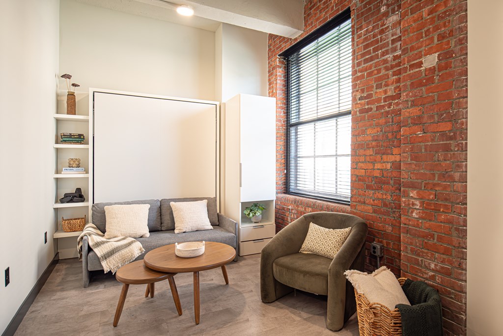 A living room with a grey couch, a brown chair, a brown table and a whiteboard.