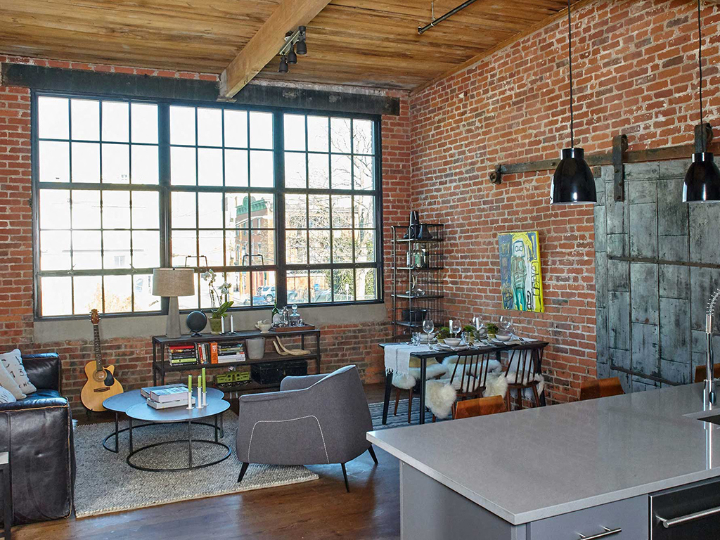 the living room and dining area of an industrial loft with brick walls and large windows