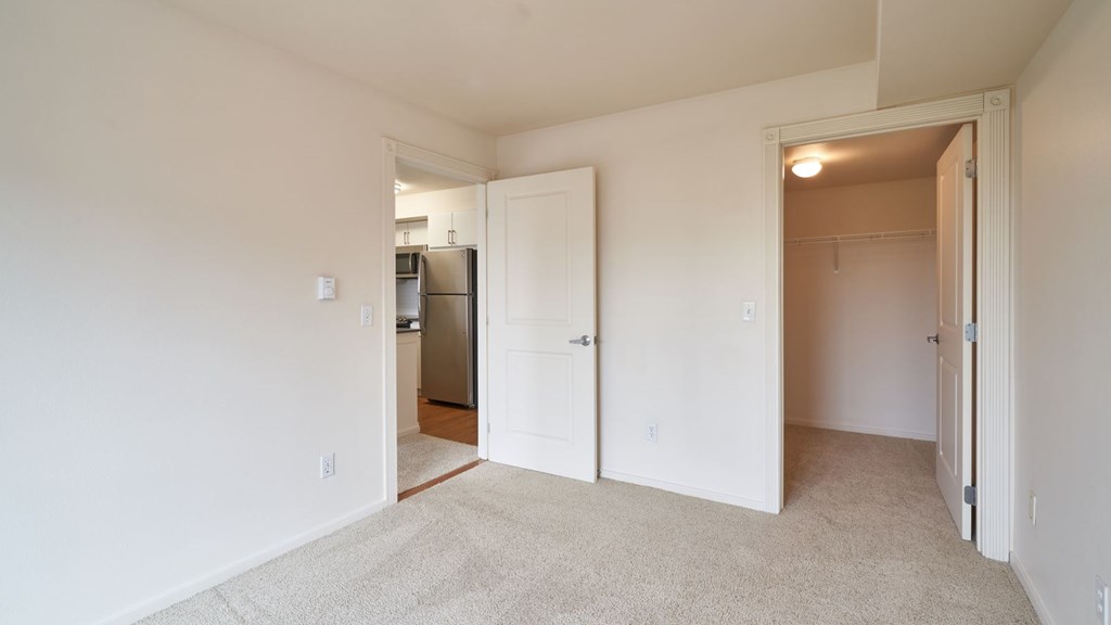 A white room with a carpeted floor and a refrigerator in the kitchen area.