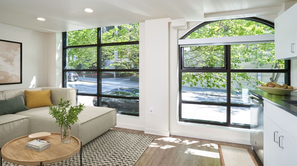 A living room with a couch, a table, and a window overlooking a street.