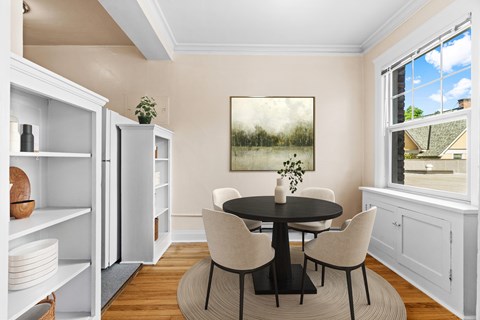 A dining room with a table set for four and a painting of a lake scene on the wall.
