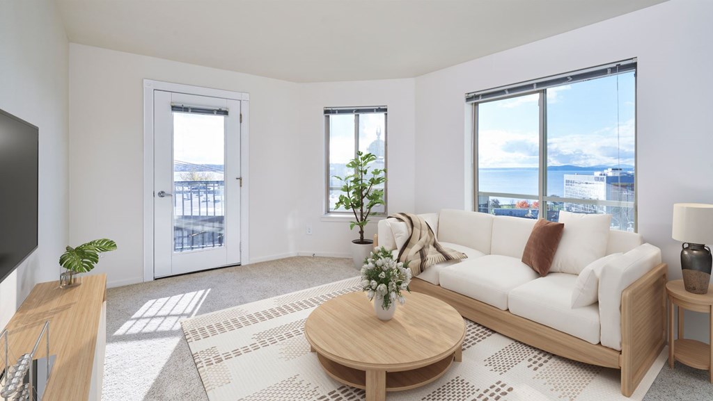 A living room with a white couch, a coffee table, and a large window overlooking the city.