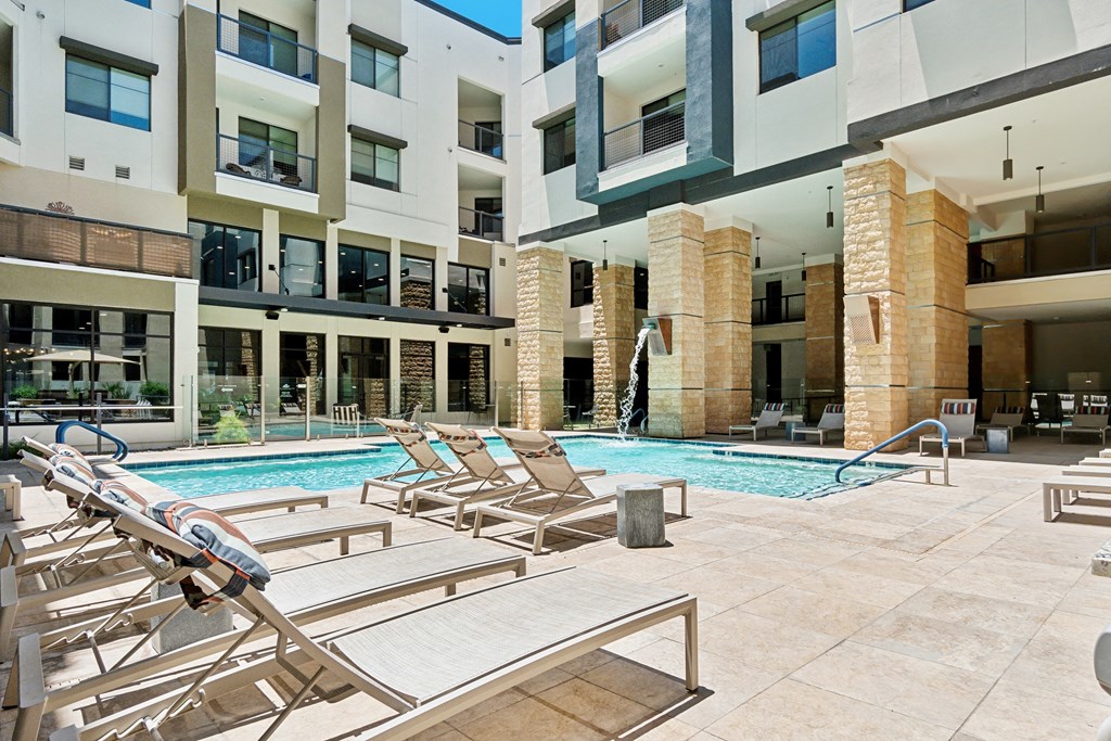 a swimming pool with lounge chairs in front of an apartment building